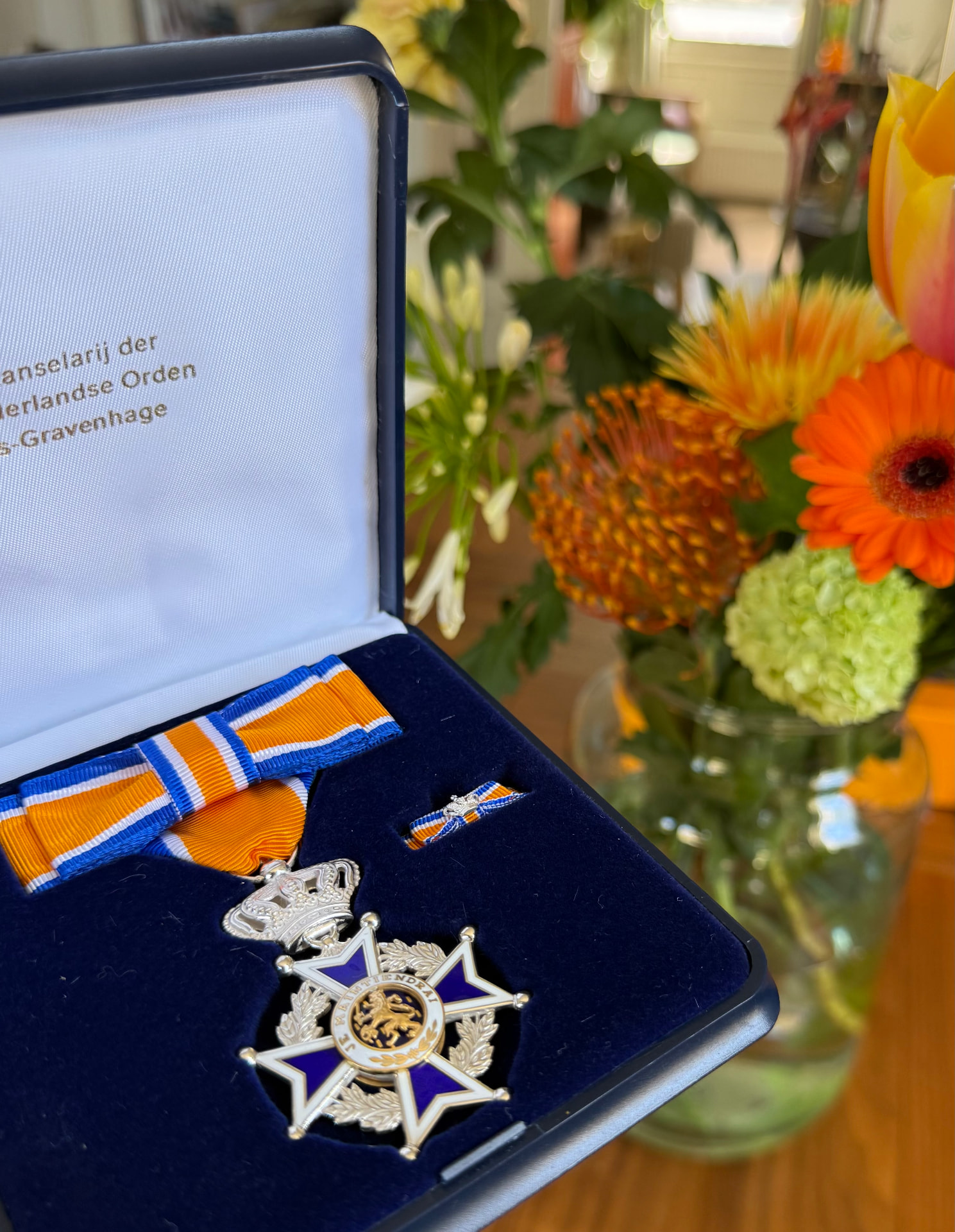 De Ridder in de Orde van Oranje Nassau in de blauwe doos, met oranje lint en bloemen op de achtergrond